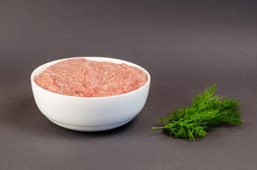 Raw ground meat and green dill on a gray background. White ceramic bowl with minced turkey. Food, ingredients.