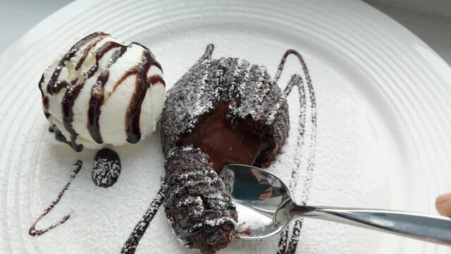 Eat french brownie cake with ice cream. Chocolate dessert. Spoon moving. Restaurant white dish. Bakery cuisine