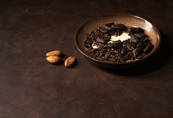 Organic cocoa beans in a small bowl on a brown background. Ingredients for baking and cooking