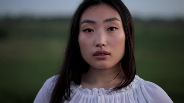 Close up of Womans Face. Portrait shot of attractive young asian woman standing in green field. Portrait of gorgeous girl looking to camera