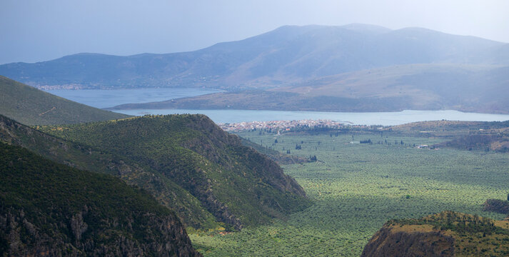 Panoramic view of the resort town of Delphi in the Parnassus Mountains, the valley with olive gardens and the Gulf of Corinth on a rainy day in Greece