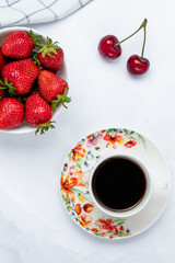 A cup of black coffee and strawberries on a white table. Hot morning drink. Red berries, breakfast concept. Summer wallpaper, background. Healthy vegetarian food. Top view. Flat lay composition.