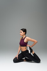 Fototapeta premium young woman in black sportswear stretching on grey background.