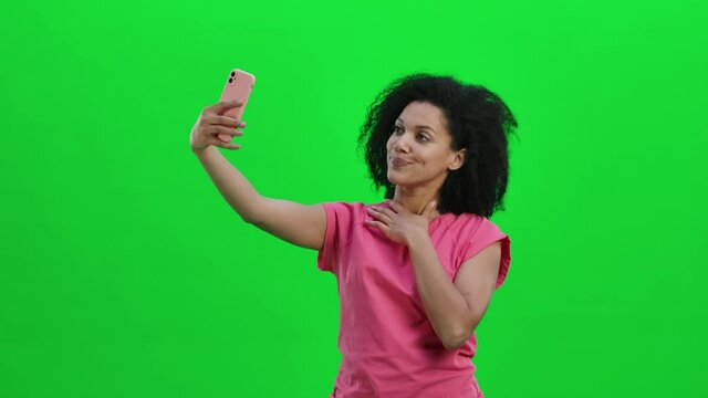Portrait of young female African American making selfie on mobile phone. Black woman with curly hair poses on green screen in the studio. Close up. Slow motion ready 59.97fps.