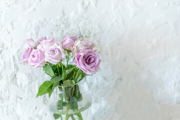 bouquet of pink roses in a transparent vase on the background of a white textured wall