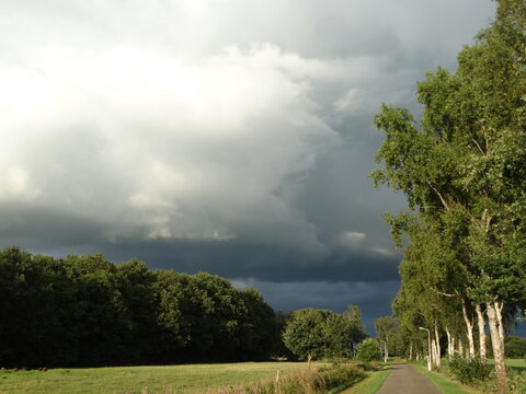 Thunder clouds. Dramatic dark sky in green summer landscape. Panoramic view on thunderstorm. Background. Onweerswolk. Code geel. Code oranje. Dreigende wolk boven groen zomer landschap.