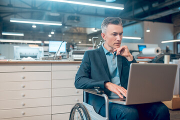 Pensive man in wheelchair looking at laptop