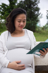Obraz premium Asian Pregnant Woman reading book in the park