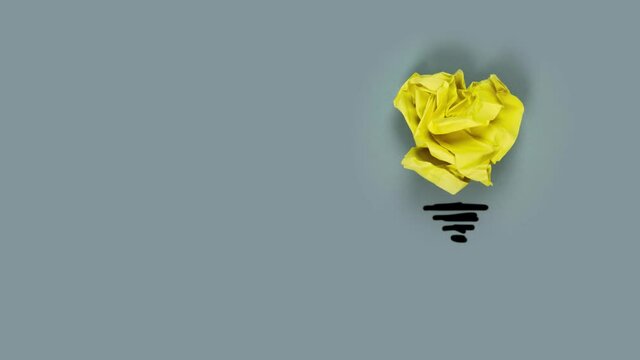 Paper being crumbled into a yellow light bulb on gray background. Concept of Innovation and Creativity. High quality 4k video.