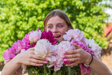 Fototapeta premium Beautiful and happy young girl in the summer with a beautiful bouquet of peonies in nature