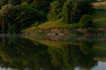 beautiful summer landscape of trees reflected in the water of the lake in a field between the hills