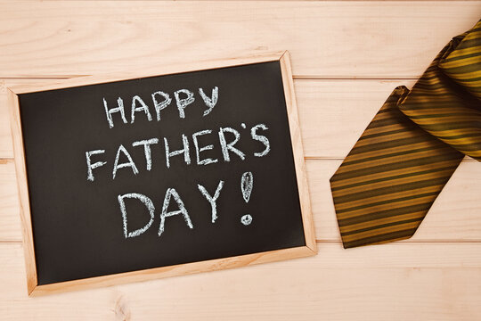 Happy fathers day on chalk board and colorful tie laid on wooden light backround.