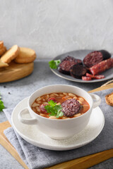 Asturiana traditional fabada with haricot, blood sausage served fresh crispy toast on gray table. Vertical orientation. Spanish cuisine.