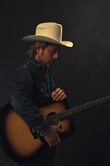 Obraz premium Man in denim shirt and white cowboy hat with acoustic western guitar in front of a grey wall.