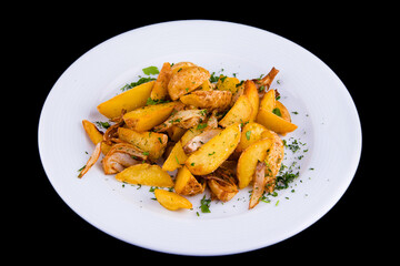 Rustic baked potato slices with onions on a white plate, isolated on a black background