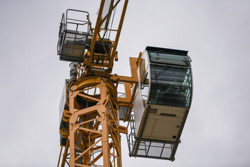 Closeup view of the control cabin of a yellow construction tower crane. Construction crane against cloudy sky.