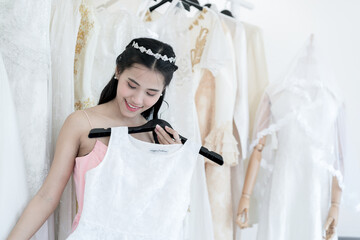 Pretty asian woman choosing and trying on dress in a Wedding dress shop. Happy Bride portrait concept