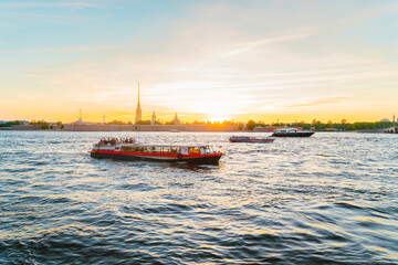 Fototapeta premium Panoramic view of the beautiful sunset over the Neva River in St. Petersburg and pleasure boats with tourists. Saint Petersburg, Russia - 05 Apr 2021