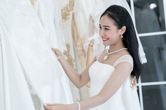 Pretty Asian Woman Choosing And Trying On Dress In A Wedding Dress Shop. Happy Bride Portrait Concept