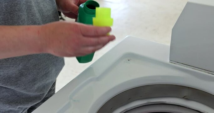 Woman pouring washing powder into the washing machine tank with laundry room