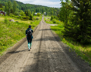 Girl walking down gravel road with green fields and forest scenery on the sides. High Coast area, northern Sweden
