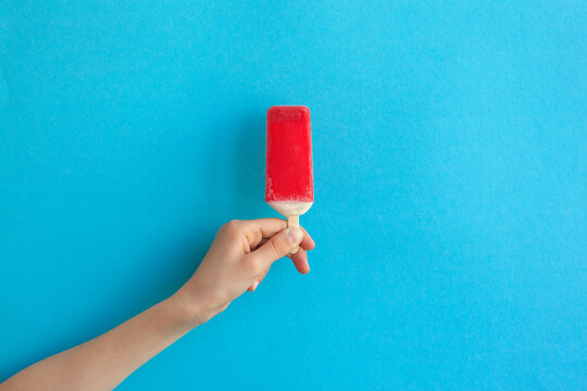 Child Hand Holding Red Ice Cream Popsicle On Blue Color Background