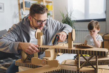 Father making cardboard airplane for his toddler son