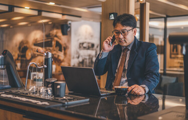 Asian businessman wearing suite and eyeglasses drink coffee , typing notebook for work at cafe restaurant. 