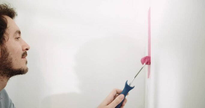 DIY Man paints a wall pink with a small roller