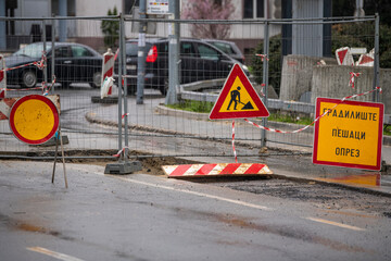 Inner city road closed by signs and boundary around street works. Construction and road work sign in downtown. Caution symbol, work in progress. Translation:''Pedestrians caution!''