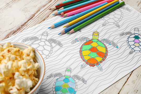 Coloring picture, popcorn and pencils on wooden background
