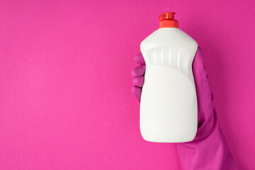Photo of hand in pink glove holding white gel detergent bottle without label on isolated pink...