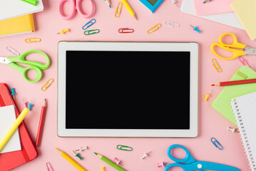 Top view photo of multicolor stationery pencils pens clips calculator reminders scissors and tablet computer display in the middle on isolated pastel pink background with copyspace