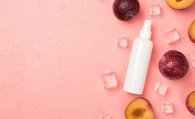 Top view photo of white spray bottle without label halves and whole plums ice cubes on the right...