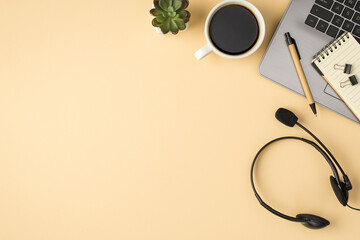 Overhead photo of laptop notebook pen paperclips plant cup of coffee and headphones isolated on the beige backdrop with copyspace
