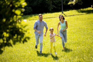 Fototapeta premium Happy young family with cute little daughter running in the park on a sunny day