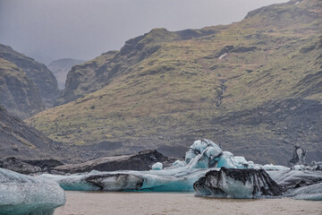 The Solheimajokull Glacier in Iceland showing icebergs and calved ice in the lagoon as ice calves...