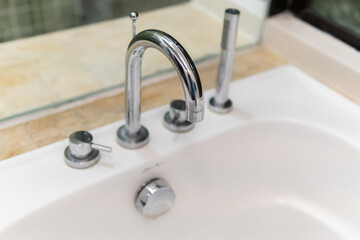 Clear water is running from shiny faucel into the sink in bathroom, closeup view. Water system in residental real estate concept.