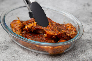Lamb chops with a mint sauce marinade in a glass dish with kitchen tongs.  On a concrete background