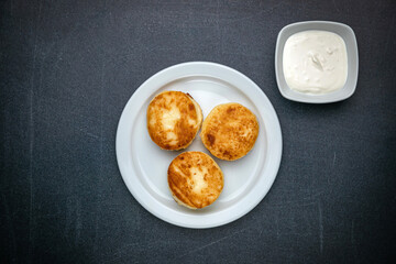 Cheesecakes on a dark table with sour cream
