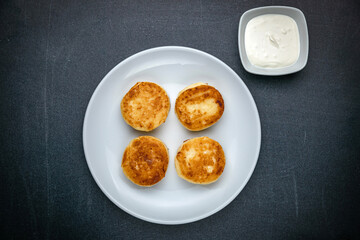 Cheesecakes on a dark table with sour cream

