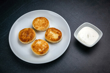 Cheesecakes on a dark table with sour cream

