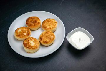 Cheesecakes on a dark table with sour cream
