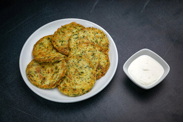 Draniki with sour cream on a dark table
