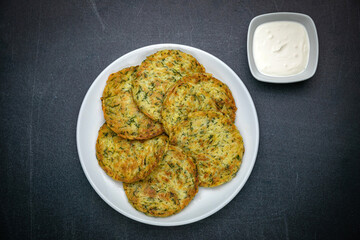 Draniki with sour cream on a dark table
