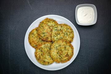 Draniki with sour cream on a dark table
