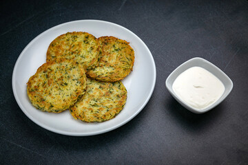 Draniki with sour cream on a dark table
