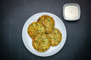 Draniki with sour cream on a dark table
