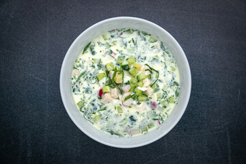 Okroshka with radish, cucumber, meat on a dark table
