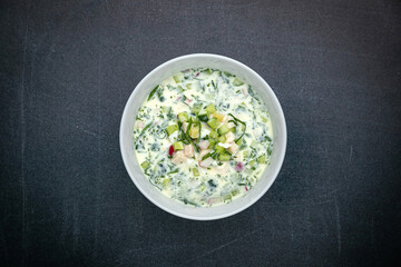 Okroshka with radish, cucumber, meat on a dark table

